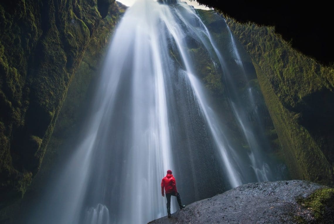 man in red poncho facing waterfall