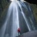man in red poncho facing waterfall