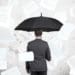 businessman holding black umbrella under falling documents