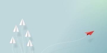 red paper airplane breaking away from group of white paper airplanes flying in formation