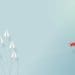 red paper airplane breaking away from group of white paper airplanes flying in formation