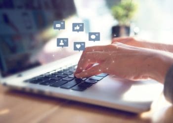 woman's hands at laptop with social media icons