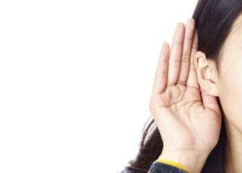 woman holding hand behind ear to hear better