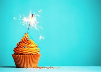 cupcake with orange frosting and sparkler candle on blue background