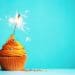 cupcake with orange frosting and sparkler candle on blue background