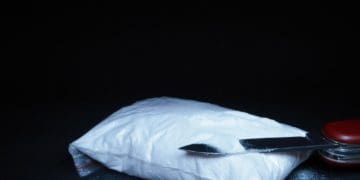 baggie of white powder and knife on black background