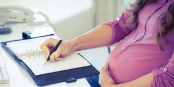 pregnant business woman at desk writing in planner