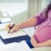 pregnant business woman at desk writing in planner