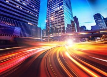time lapse photo of speeding cars against a city skyline