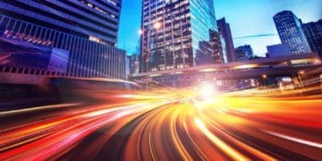 time lapse photo of speeding cars against a city skyline