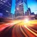 time lapse photo of speeding cars against a city skyline