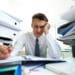 Man frustrated at desk by large amounts of paperwork
