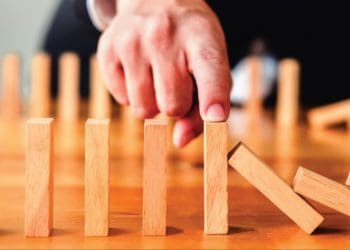 index finger places atop wooden block to signfy domino effect