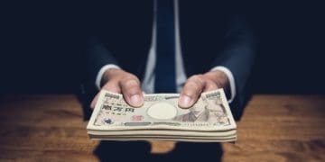 anonymous businessman handing bribe in yen from the shadows