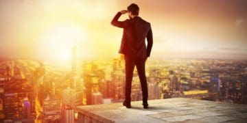 businessman on building rooftop shielding his eyes and looking at the horizon