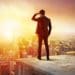 businessman on building rooftop shielding his eyes and looking at the horizon