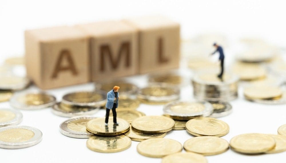 miniature people standing on coins beside wooden blocks spelling AML