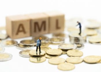 miniature people standing on coins beside wooden blocks spelling AML