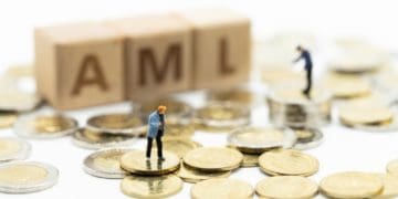 miniature people standing on coins beside wooden blocks spelling AML