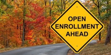 yellow "open enrollment ahead" sign posted on road in autumn