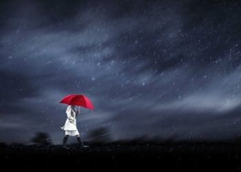 woman in white trench with red umbrella set against dark stormy skies