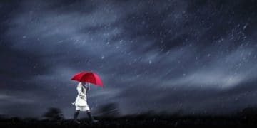 woman in white trench with red umbrella set against dark stormy skies