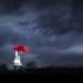 woman in white trench with red umbrella set against dark stormy skies