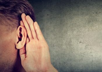 man holding hand behind his ear to hear more clearly