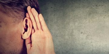 man holding hand behind his ear to hear more clearly