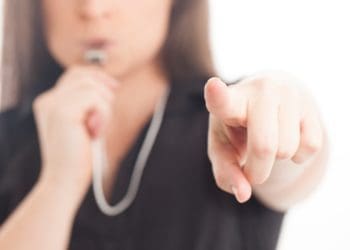 businesswoman in black blowing a whistle and pointing at the camera