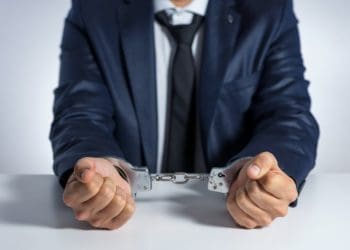 man in navy suit in handcuffs