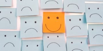 orange post-it with happy face surrounded by gray post-its with sad faces
