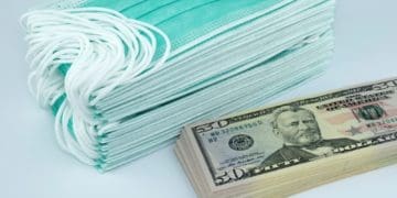 stack of cash beside stack of medical masks