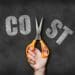 hand with scissors cutting the word "cost" in half