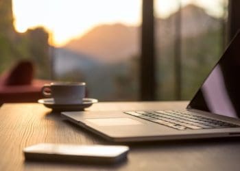open laptop on table with view overlooking mountains