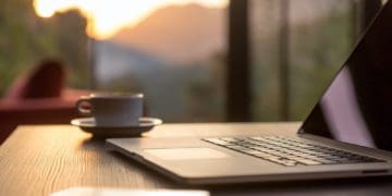 open laptop on table with view overlooking mountains