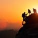 team helping one another climb a mountain at sunset