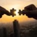 silhouette of hands connecting jigsaw puzzle pieces with sunset in background
