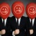 businessmen holding red balloons with various emoji faces