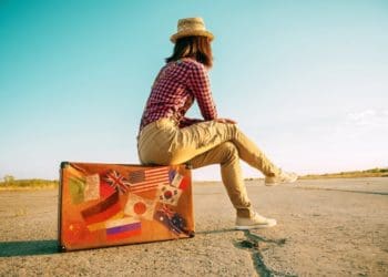woman on the road sitting on suitcase marked with travel stickers