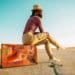 woman on the road sitting on suitcase marked with travel stickers