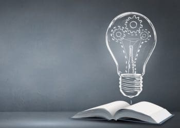 open book and illustration of light bulb against blackboard background