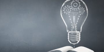 open book and illustration of light bulb against blackboard background