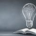open book and illustration of light bulb against blackboard background