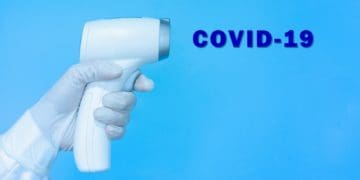 doctor wearing gloves, holding medical infrared forehead thermometer for screening body temperature with text Covid-19