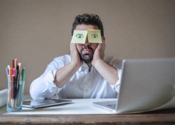 man sleeping at laptop with post-it eyes