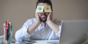 man sleeping at laptop with post-it eyes