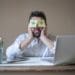 man sleeping at laptop with post-it eyes