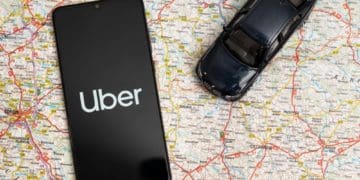 smartphone with uber app open and toy black car on open road map
