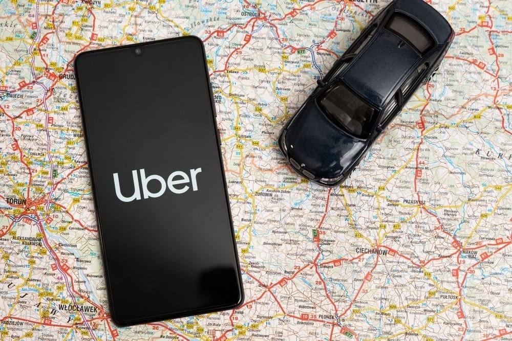 smartphone with uber app open and toy black car on open road map